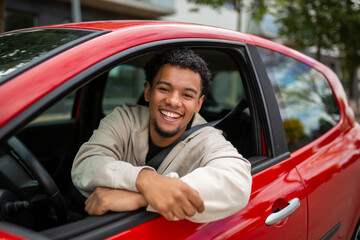 Smiling young man in red car leaning out of window