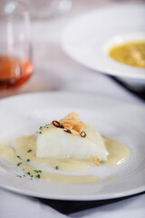 Dish of delicious cod fillet with a sauce and some garlic and pepper on top of it with rose wine at background.