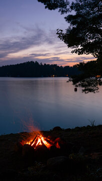 View of tranquil Brantingham Lake at sunset with serene reflections and a campfire, Brantingham, United States of America.