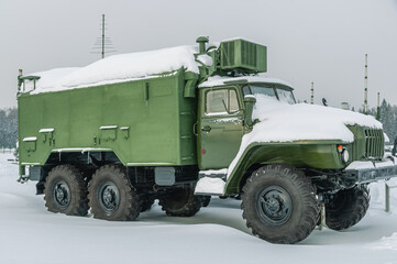 Obraz premium A military truck with a body for transporting people and goods. A military truck stands in snowdrifts in winter. A three-axle army all-terrain truck in the snow during a snowfall.