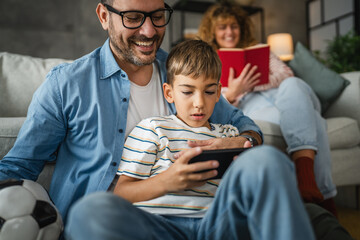 dad and son and play video games on cellphone with mum behind