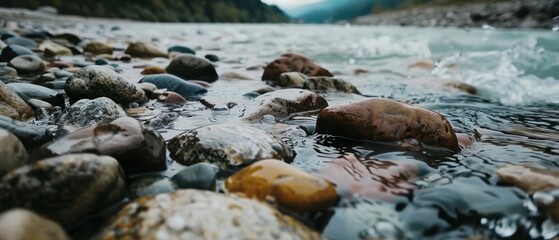 Fototapeta premium Dark, smooth stones lie next to a rushing river, encapsulating nature's raw and untamed beauty by the water's edge.