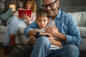 dad and son and play video games on cellphone with mum behind