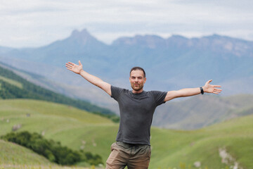 A man stands confidently atop a majestic hill with his arms stretched wide, embracing the beauty of the vast landscape around him