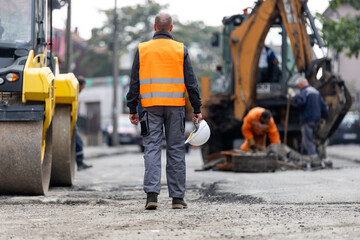 Construction workers repair a road with heavy machinery in an urban environment during the day, ensuring smooth traffic flow and safety