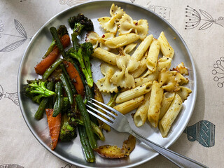 Penne and Farfalle pasta with saute vegetables on the steel plate with fork