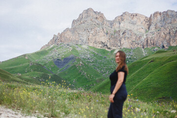 A woman is gracefully standing in a lush green field, with a majestic mountain prominently rising in the background under a clear sky