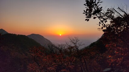 Dramatic sunset and sunrise with sun flare over mountain valley morning twilight evening sky. The incandescent round sun goes into the sunset.