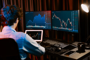 Young investor stock trader searching on laptop comparing with dynamic exchange rate screens of current market graph online in real time at neon light modern office, analyzing financial data. Gusher.