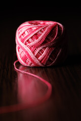 A skein of colored melange pink threads lies on a dark wooden table. Selective focus.