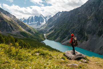 A tourist girl stands on a stone overlooking the beautiful mountains and Lake Shavlinskoye. Altai....