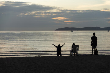 Obraz premium Silhouette of a family of three relaxing by the sea waiting for the sun