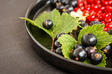 Close-up of black currants in a black bowl with green leaves. Organic berries mix, cropped, close up, food photography for food blog, copy space for text