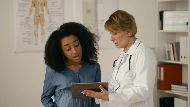 Female doctor showing baby ultrasound image to smiling pregnant woman, check-up