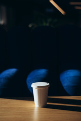 Paper cup of coffee on wooden table against blurred background cafe of interior.