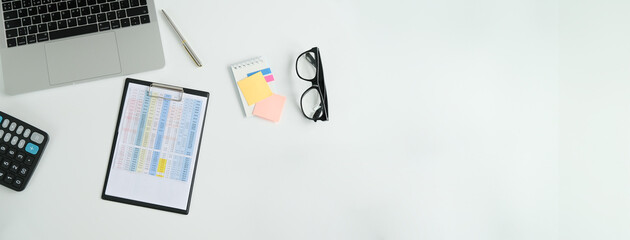 Top view of a laptop computer, a notebook for notes and a calculator on a white table with a place to copy