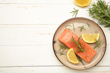 Red fish. Raw salmon fillet with rosemary and lemon on grey plate on white background.