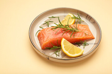 Red fish. Raw salmon fillet with rosemary and lemon on plate on beige background.