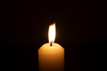 A single burning candle flame or light glowing on a big white candle isolated on red or dark background on table in church for Christmas, funeral or memorial service