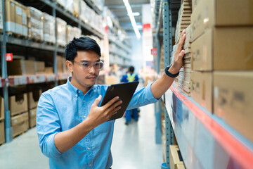 A man in a blue shirt is looking at a tablet while standing in a warehouse. He is likely checking...