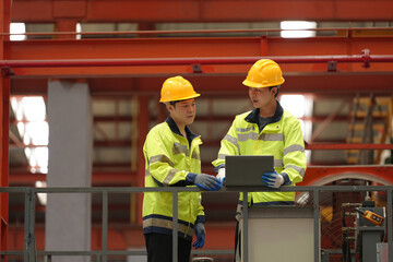 two professional engineer, worker, technician use clipboard discuss work, walk in steel metal manufacture factory plant industry. Asian man and woman wear hard hat check quality machine