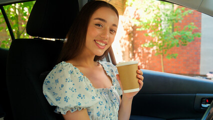 Happy satisfied Caucasian woman driver female client buyer owner girl drinking coffee cup touching car new automobile wheel enjoying morning routine going to work looking at camera smiling inside auto