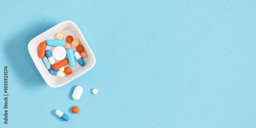 Wall mural Variety of pills and capsules. Porcelain pill container with scattered capsules and tablets on light blue background representing medical and pharmaceutical concepts.Top view. Flat lay.