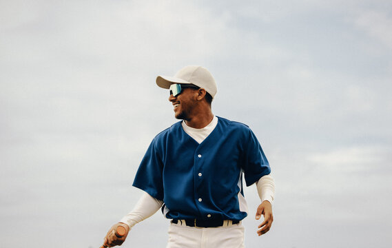 Joyful professional baseball player in blue jersey with cap smiling on the field