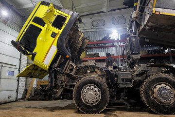 Inside a spacious garage, a bright yellow dump truck is currently undergoing repairs and...
