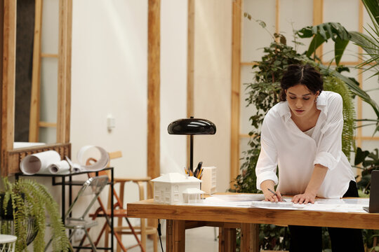 Architect reviewing architectural plans in bright modern office surrounded by greenery and design elements