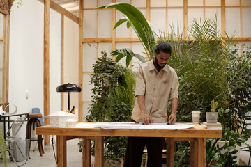 Architect focusing on architectural drafts in office filled with plants and natural materials
