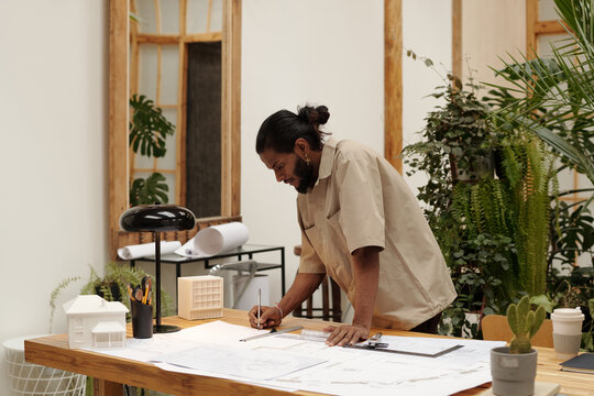 Architect focusing on detailed building plans while surrounded by plants and models