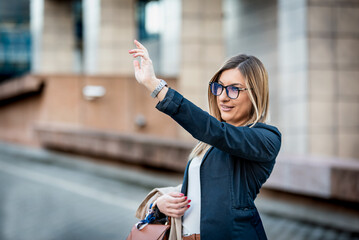 Portrait of a confident beautiful businesswoman raising arm for taxi in the city. Attractive young woman calling a cab after work.