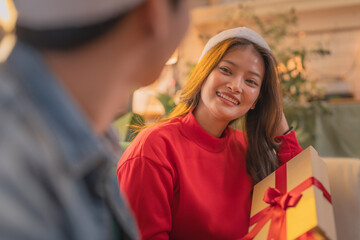 A joyful woman in red sweater and festive hat smiles while holding beautifully wrapped gift, creating warm and cheerful holiday atmosphere