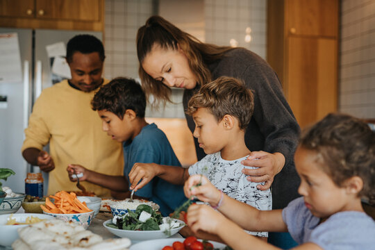 Parents teaching children to cook food in kitchen at home - Powered by Adobe