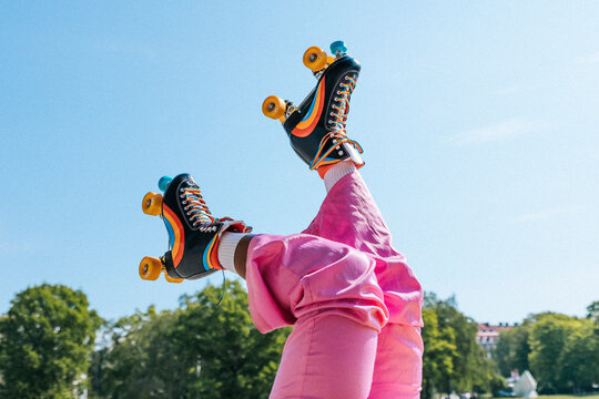 Low section of woman wearing rainbow striped roller skates under blue sky