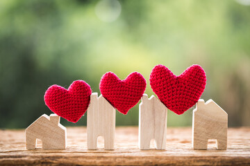 ็A red heart is placed between wooden houses model put on the old wood on sunlight in the public park, The buying for change or expand a new real estate as a gift to family or the one loved concept.