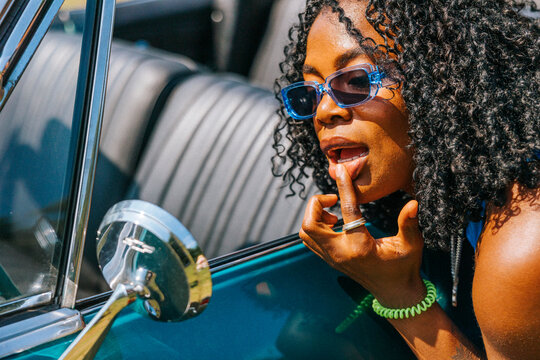 Curly hair woman wearing sunglasses looking in side-view mirror of car