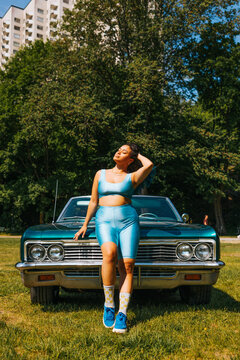 Young vuluptuous woman with hand in hair standing in front of car at sunny day