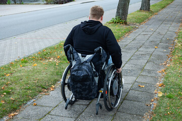 Junger Mann fährt im Rollstuhl, unebener Gehweg neben einer Straße