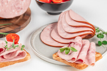 Plate of tasty sandwiches with boiled sausage and tomato on white table