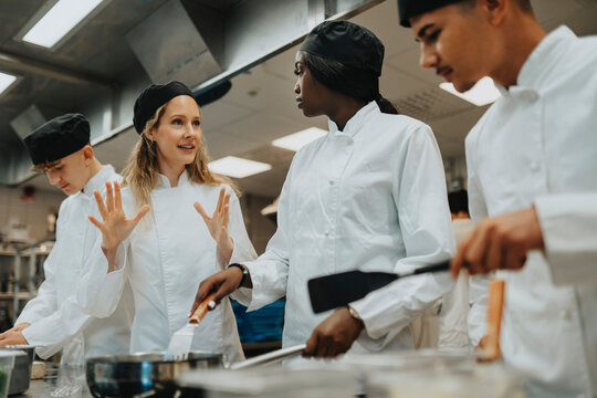 Teacher gesturing while guiding male and female trainee at culinary school