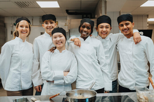 Portrait of happy male and female trainee standing with teacher at restaurant high school