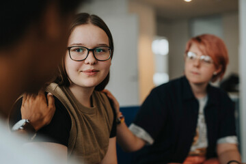 Teenage girl being console by male and non-binary friend during group therapy