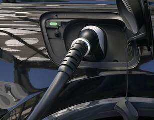 electric black car plugged to charge battery, close up of the plug. Clean energy, electric vehicle detail during recharge. sustainable transport