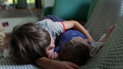 Two young siblings lying on a couch, snuggling closely, showing a moment of affection and bonding in a cozy home environment, with natural light filling the room