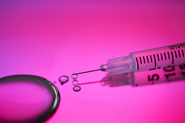Injection syringe with a drop of drug on a rich pink background.
