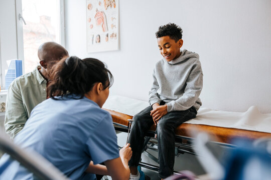 Female pediatrician checking knee of boy with reflex hammer in medical examination room