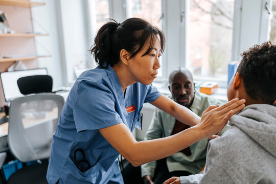 Female pediatrician checking neck ache of boy in medical examination room