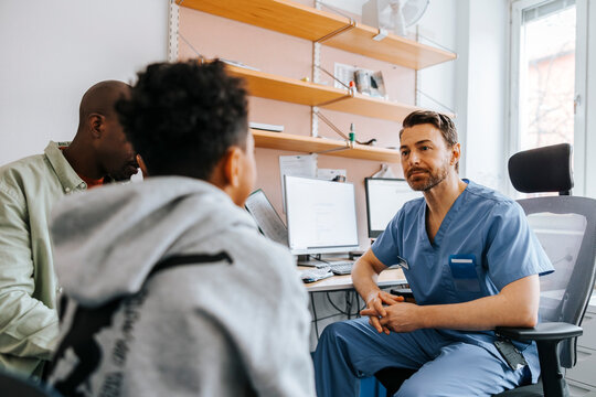 Male pediatrician listening to boy's problems while sitting on chair in medical examination room